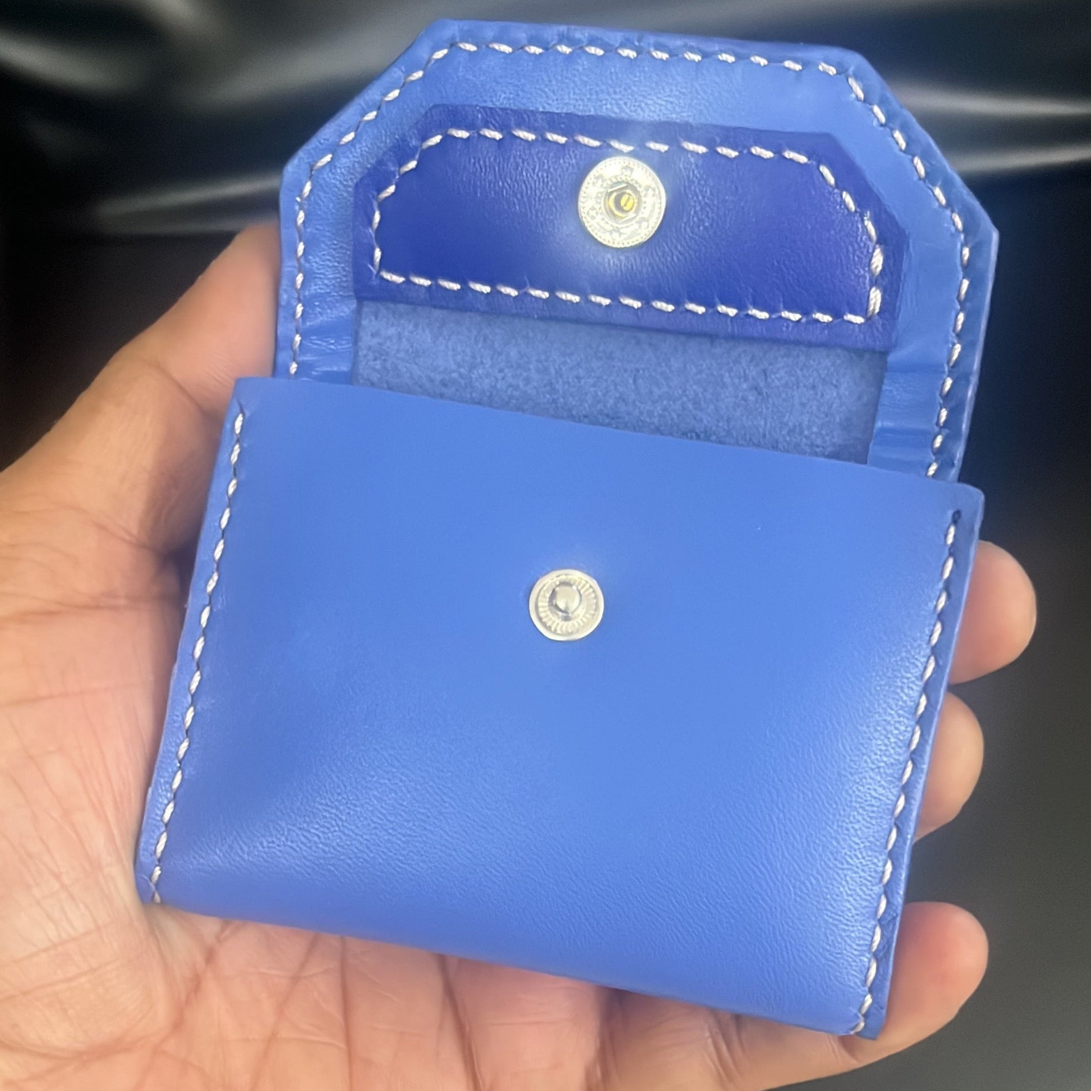 Hand holding a blue leather wallet with a brand logo against a dark background