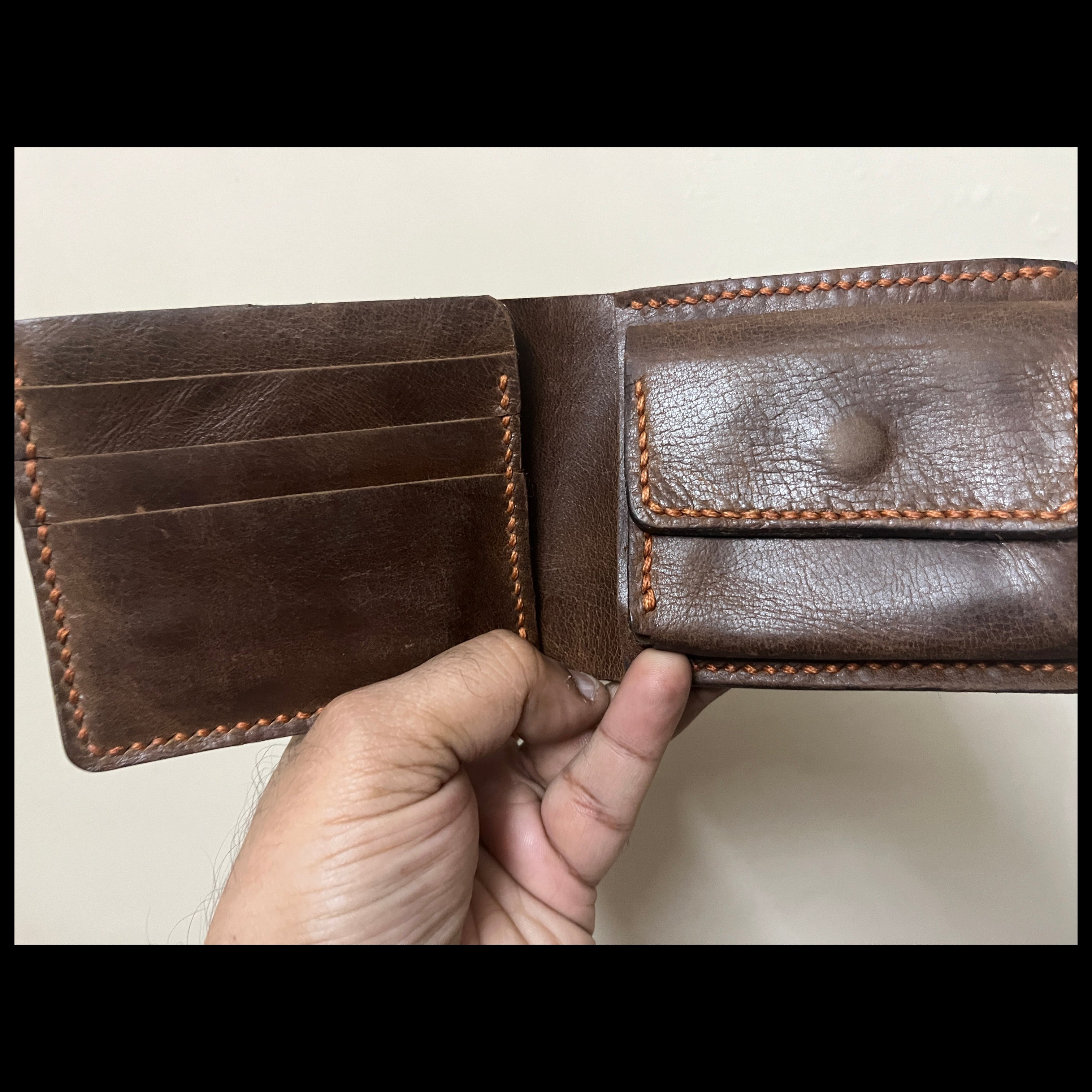Brown leather wallet held open by a hand on a light background