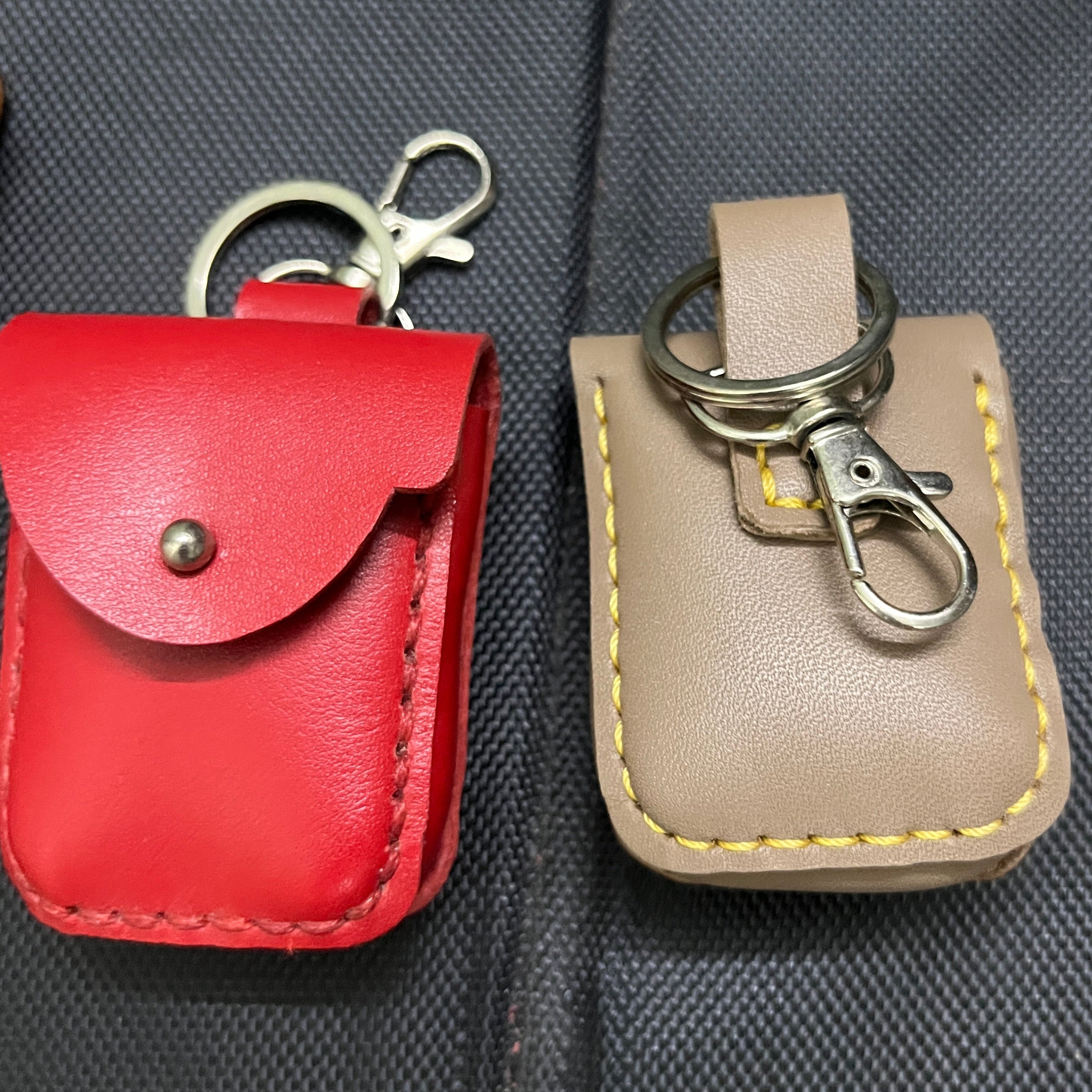 Two leather key cases, one beige and one red, attached to a black textured surface.