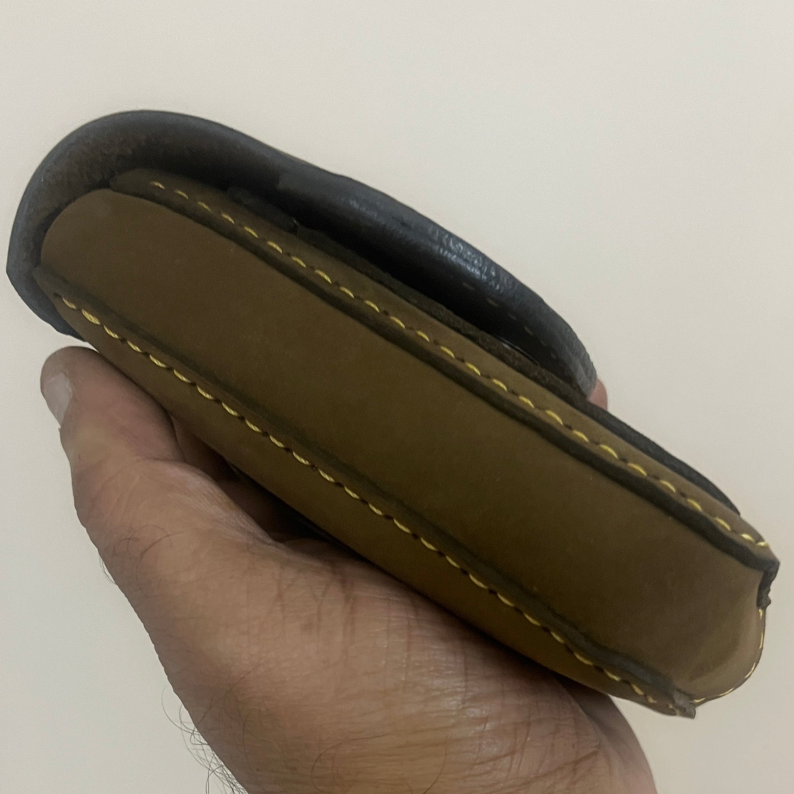 Hand holding a brown leather case with a white background