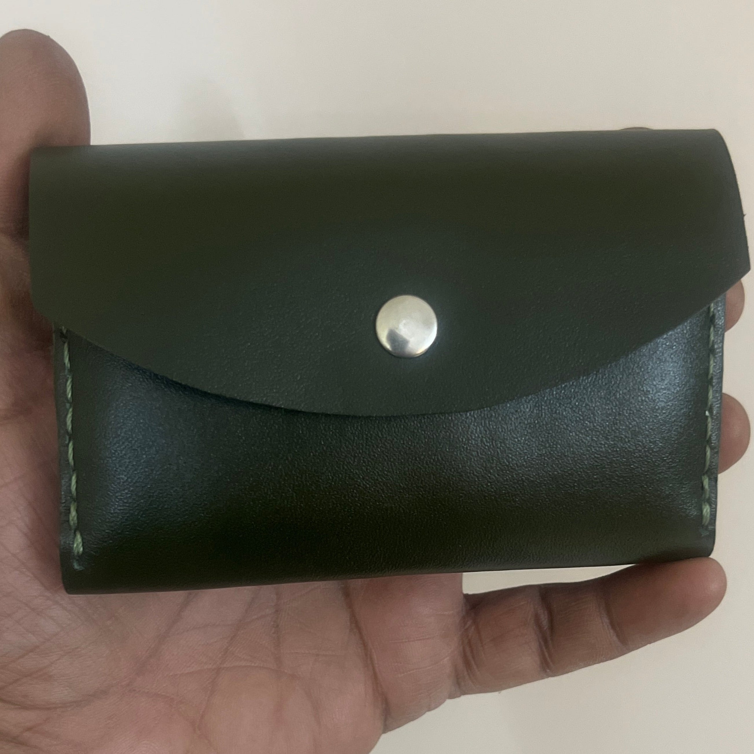 Hand holding a black leather wallet with a silver button on a plain background