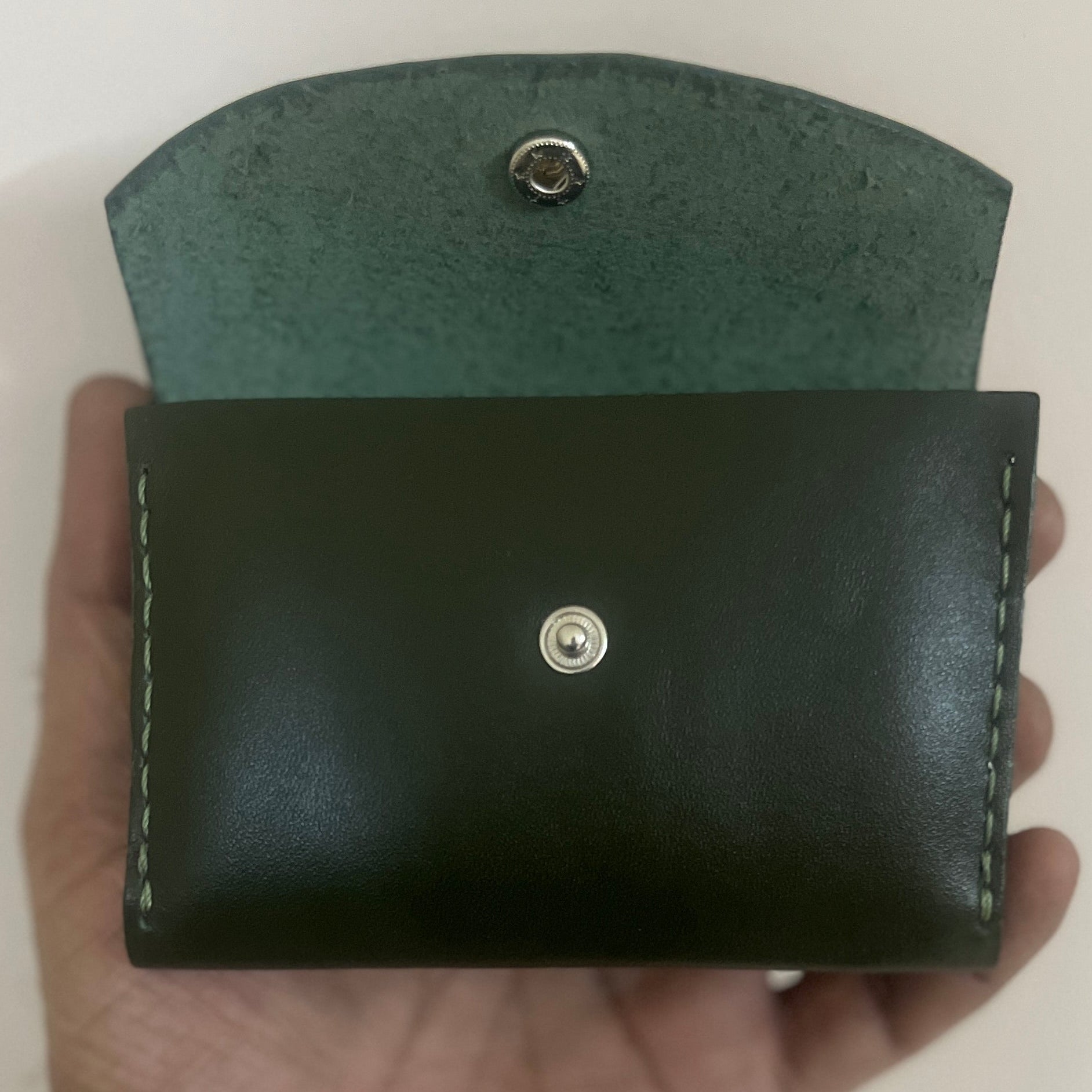 Hand holding a black leather wallet with a green textured cover against a white background