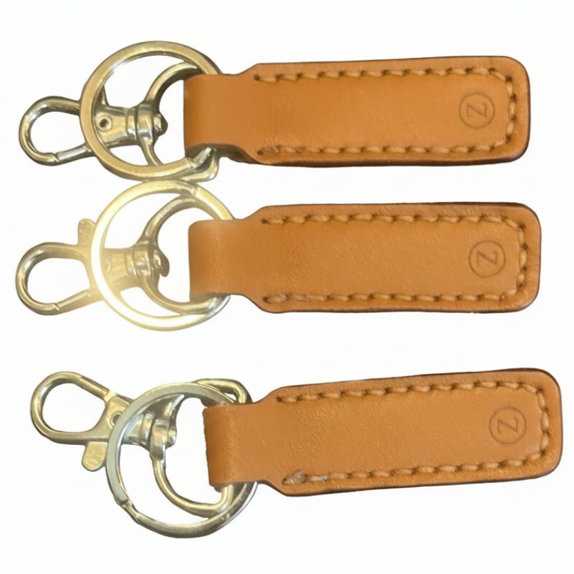 Three brown leather keychains with metal hooks on a dark textured surface