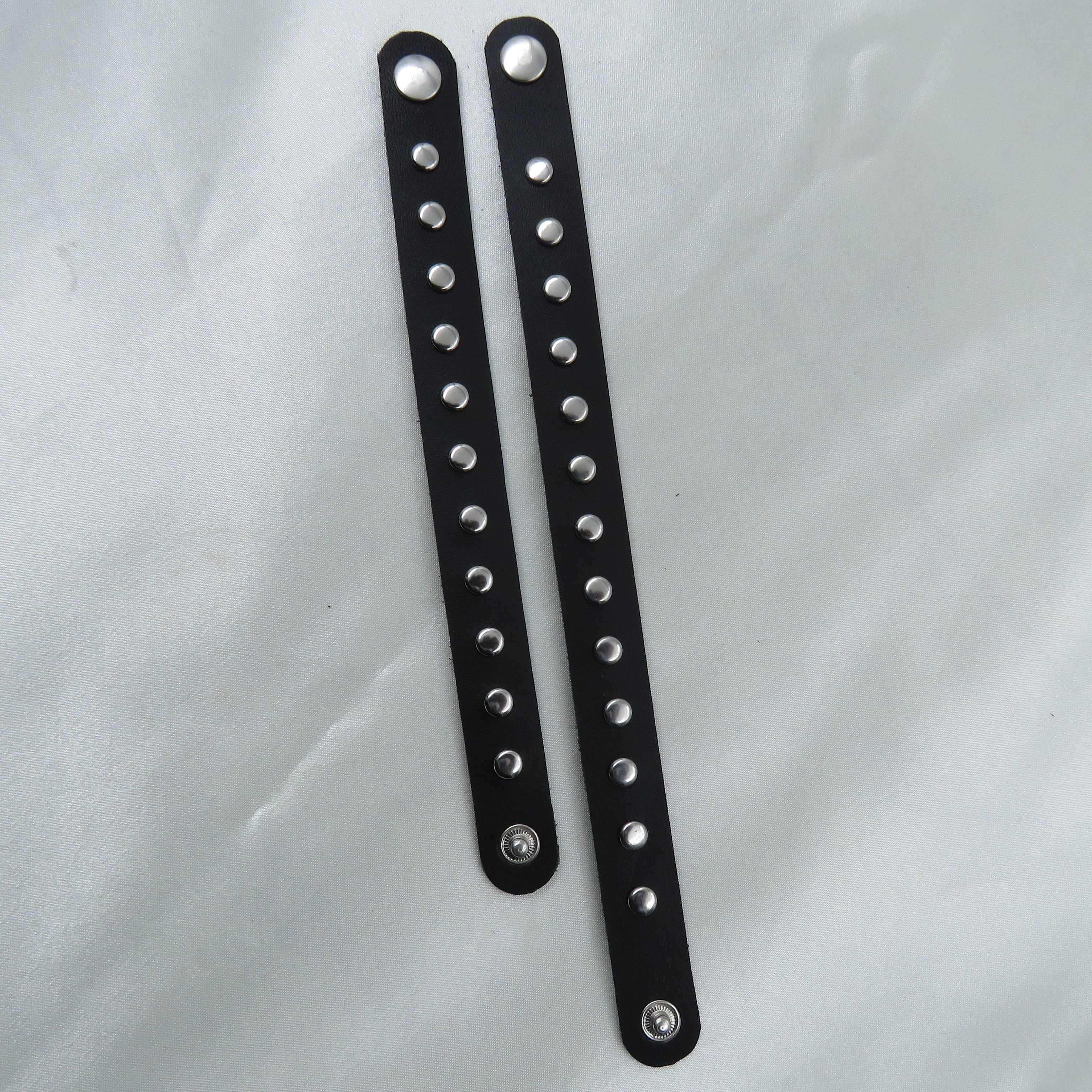 Two black leather straps with silver studs on a white background