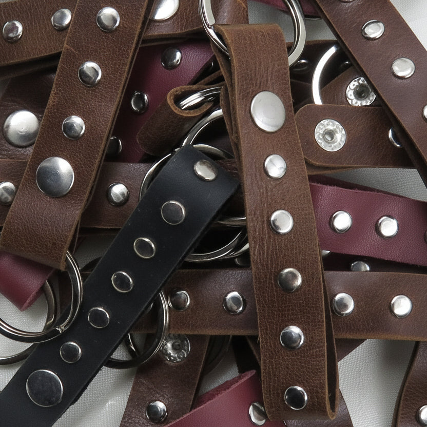 Stack of brown leather straps with silver studs and rings on a white background