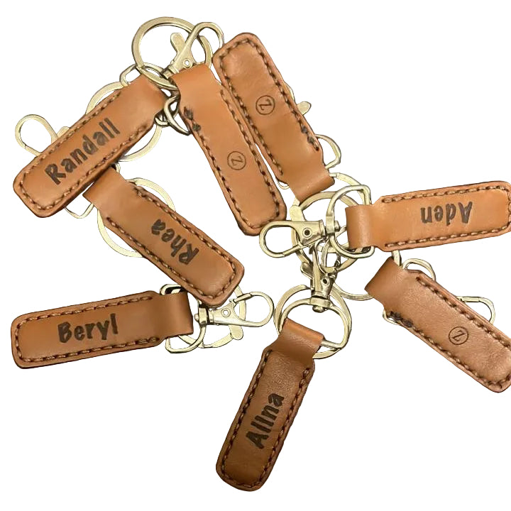 Brown leather keychains with engraved names on a dark surface
