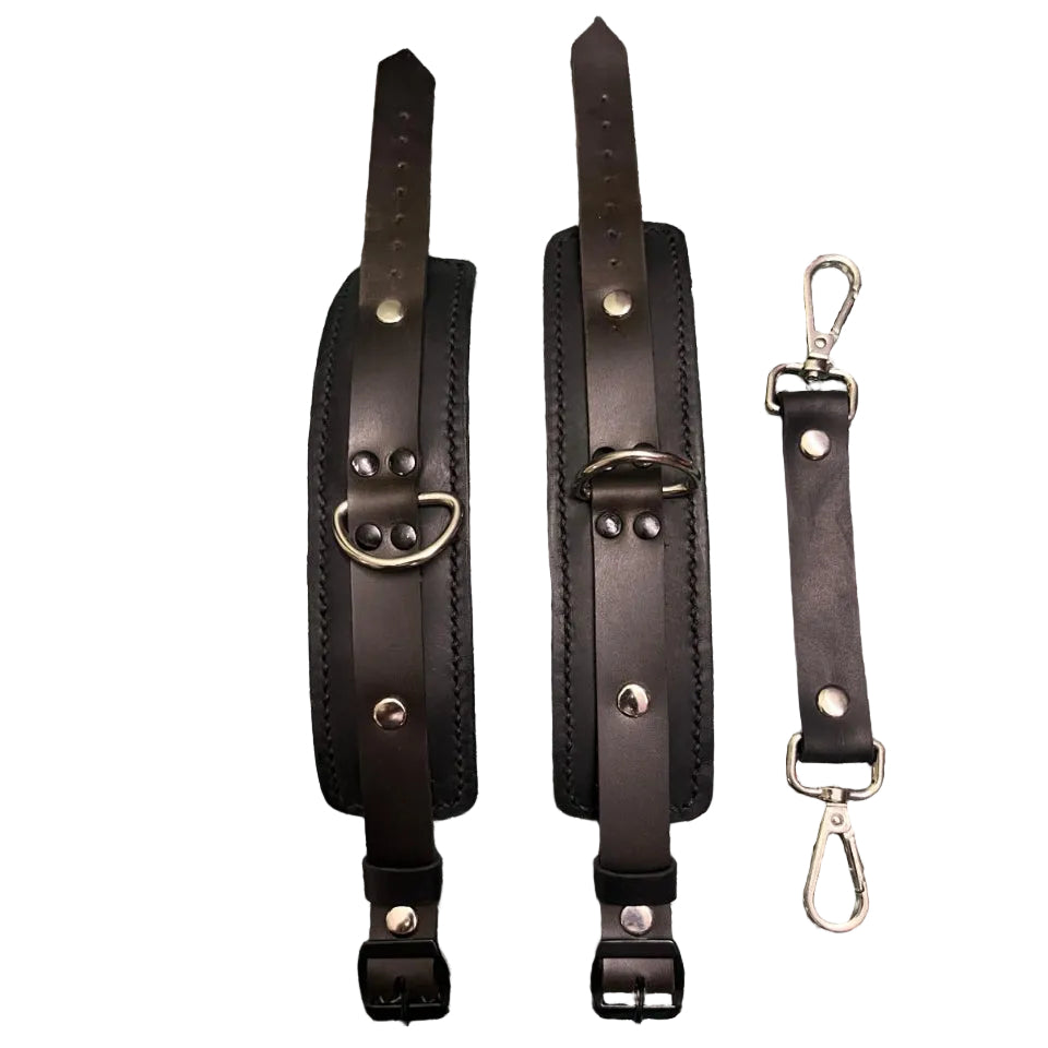 Two leather straps with metal buckles and a keychain on a green cutting mat.