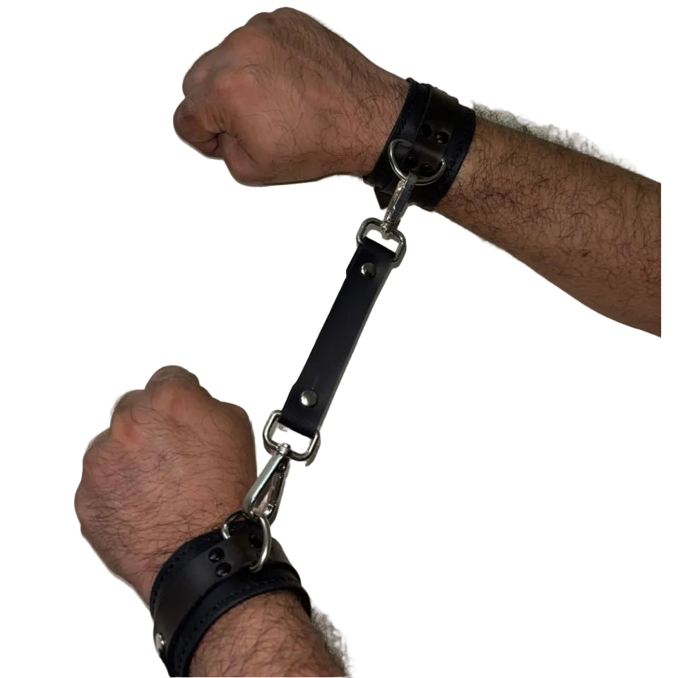 Two wrists with black leather cuffs on a plain background